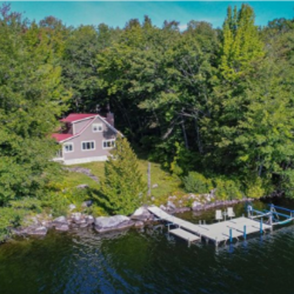 Arial wide shot of beige house to the left, dock and water to the right