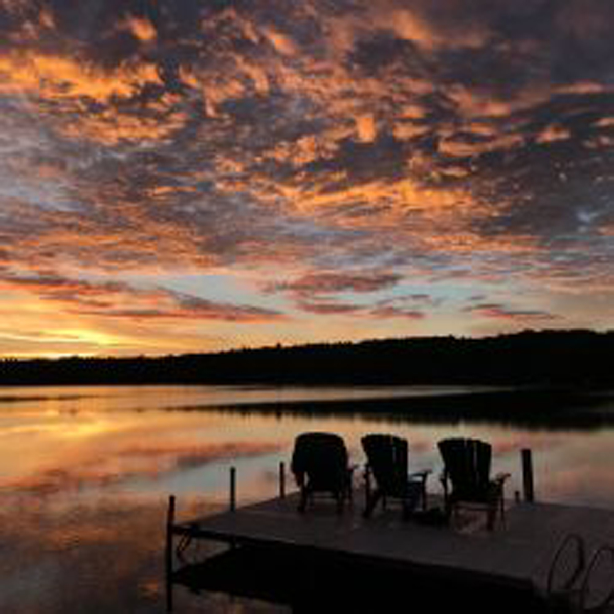 Sunset on horizon, dock with three chairs in the foreground